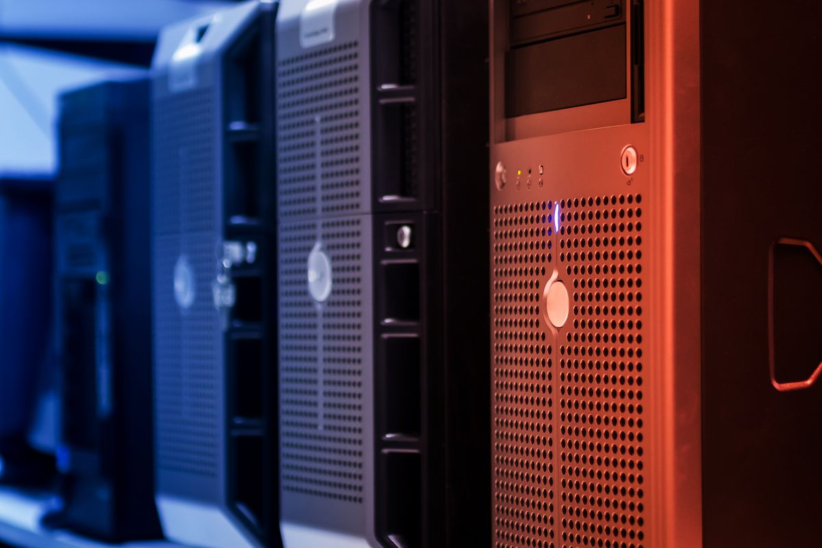 Tower servers in a data centre rack lit with blue and red indicator lights